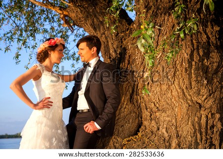 Wedding couple smiling and happy below the tree to the river bank on a beautiful sunny day