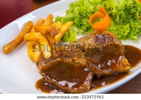 Grilled steak, french fry and salad on a white plate with restaurant background. Selective focus and shallow depth of field.