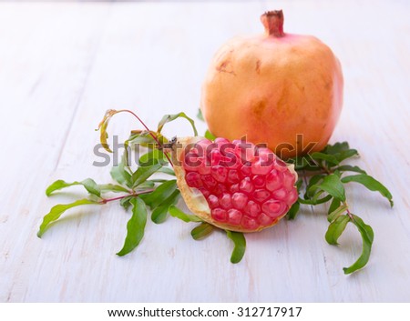 Half pomegranate and raw pomegranates on a white wooden background
