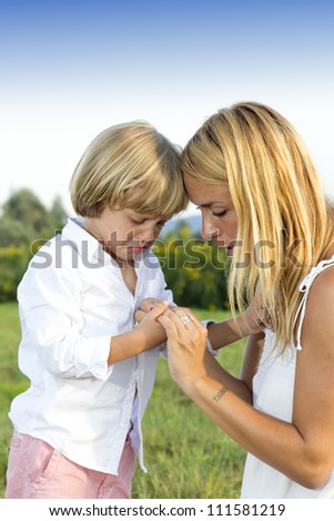 Crying young boy showing finger injury to his concerned mother, outdoors in the park
