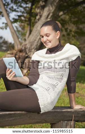 Cute smiling girl with modern tablet PC e-reader, outdoors in the park