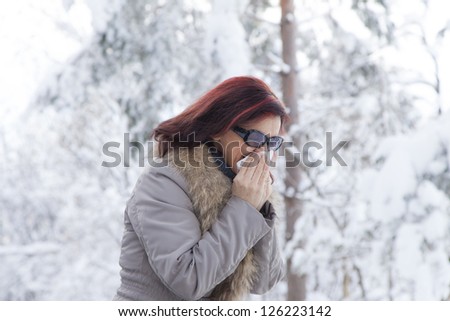 Portrait of a cute mid aged woman blowing nose-sneezing, outdoors on winter day