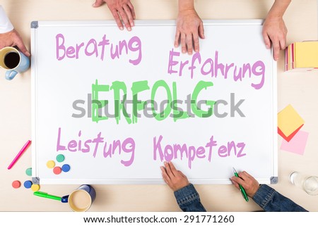 whiteboard with german business words like success, three persons, overview of an desk top