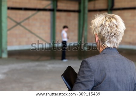 older Business woman is inspecting a warehouse, younger workmate in the background
