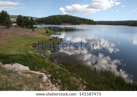 Mountain alpine lake with green shoreline and white clouds reflected in water/High Desert Alpine Lake with Cloud Reflections in Water/Mountain lake grassy shoreline with clouds reflected in water
