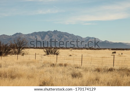 Windmill in grasslands and twin-headed peaks in mountains of semi-desert/High-desert Winter Fenced Grasslands Scenic with Windmill and Two Small Mountain Peaks/Grasslands prairie and windmill vista