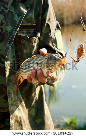 Close hands of fisher with the fish near the lake