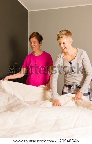 Lesbian couple make the bed in the morning, vertical format