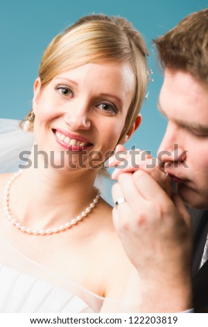 Happy smiling bride, groom kissing hand of the bride, blue background, vertical format