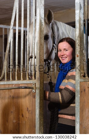 Smiling woman and white horse inside a stall, vertical format
