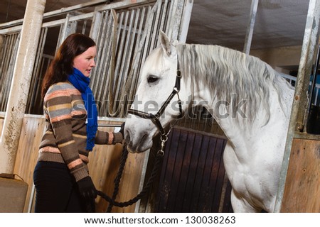 Woman and white horse inside a stall, horizon format