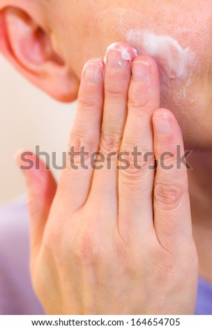 Mature woman spreading skincare cream on her cheek, vertical format