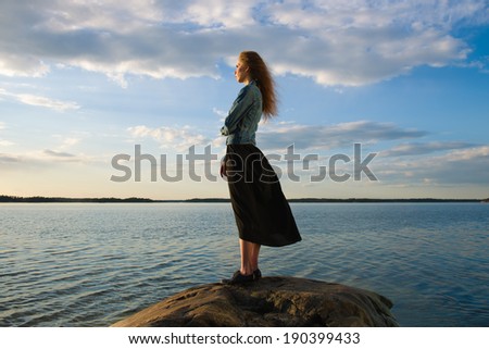 Beautiful young woman looks at the horizon on shore - wind blowing and cloudy sky