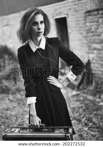 Fashionable young woman with her suitcase, old rural scene, black and white image