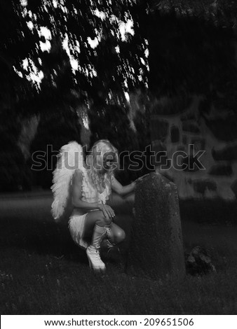 Sexy woman wearing white angel costume and wings, she leans to the tombstone - motion blurring, combination of natural and flash lights