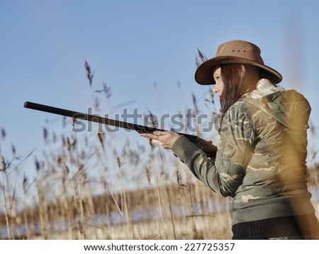 Waterfowl hunting, female hunter use the shotgun, reeds and blue sky on background