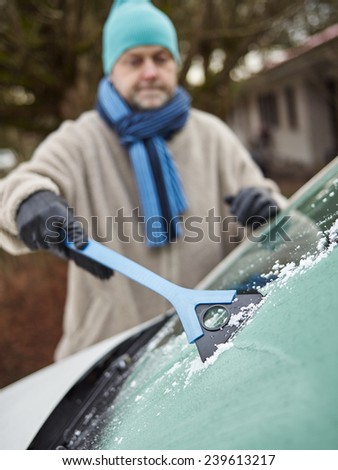 The mid adult man cleans a frozen windshield - focus on ice scraper, vertical format
