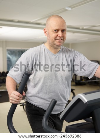 Mature man takes care of his health and he use elliptical trainer in the gym