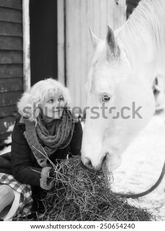 Attractive blond woman feeds a white horse, overcast winter day, black and white image, focus on horse eyes
