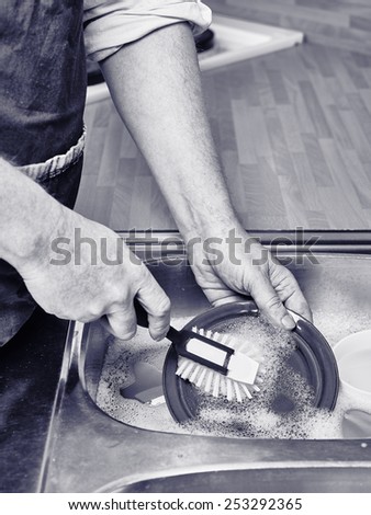 Close up, man washes dishes by hand, tinted black and white image