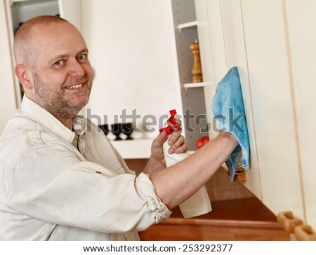 Homeworks, smiling man used a cleaning cloth and a detergent spray, he cleaning the kitchen cupboard door