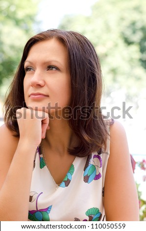 Portrait of a pensive thoughtful woman sitting outdoors with her chin on her hand as she gazes off into space