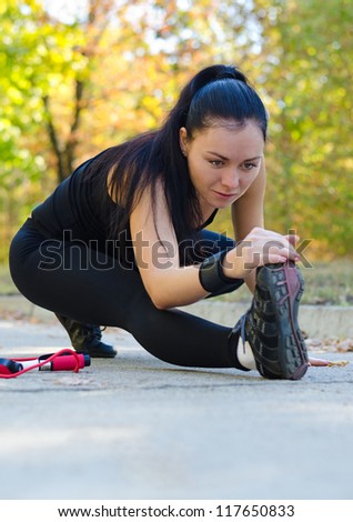 Young woman limbering up before exercising stretching low on the ground with her leg extended stretching her muscles as she touches her toes