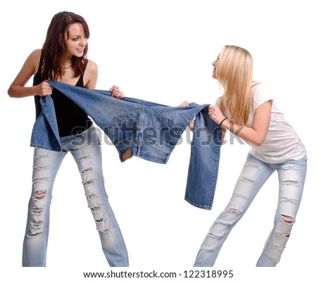Two casual young women fighting and having a tug of war over a pair of denim jeans, studio portrait isolated on white