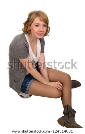 Happy casual young woman sitting on a soccer ball with her legs crossed wearing shorts and boots smiling up at the camera with a beautiful smile isolated on white