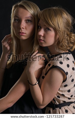 Two attractive scared young women standing close together in the shadows staring at the camera with sombre expressions