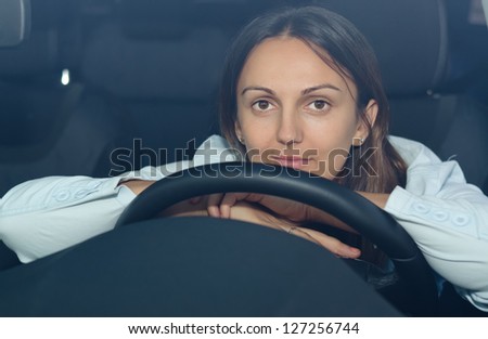 View through the windscreen of a woman waiting patiently in her car resting her chin and hands on the steering wheel