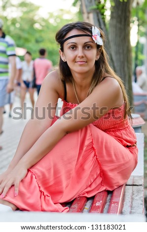 Young brunette in a red sundress sitting on a bench