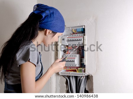 Young woman holding a screwdriver looking at an open electrical box and checking the circuit breakers