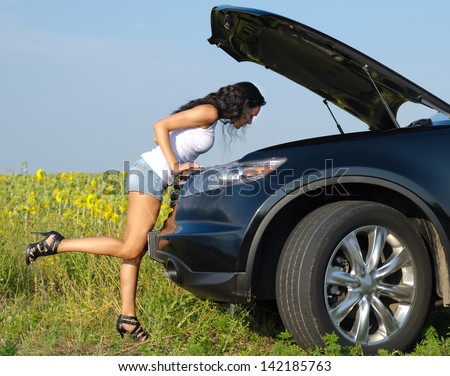 Woman in sexy shorts and stilettoes leaning over checking her car engine after breaking down in the countryside