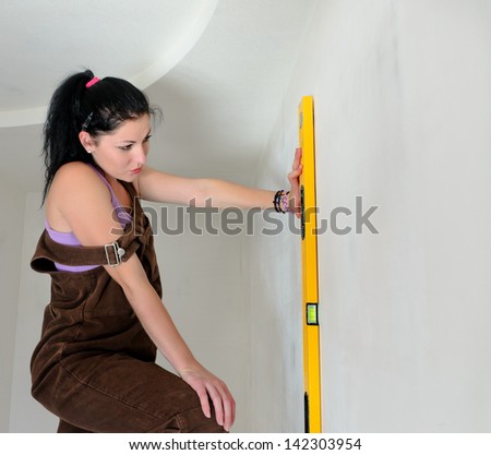 Woman finding a straight line with a spirit level holding iagainst wall in the vertical position while renovating her house