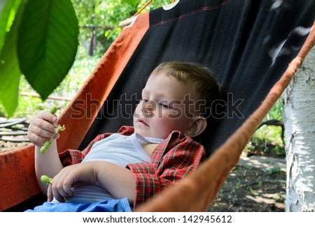 Small boy relaxing in a hammock in the summer heat in the shade of a tree in a lush garden