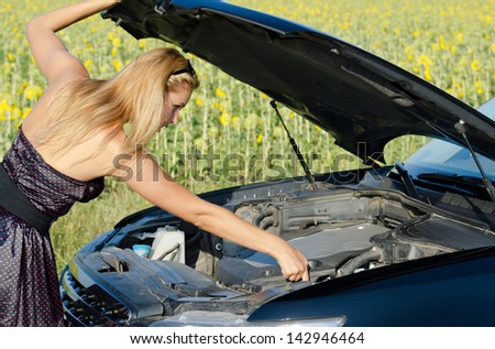 Woman leaning over under the open bonnet of the car checking the engine oil