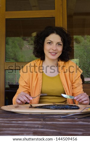 Woman enjoying a seafood meal sitting down to eat at a rustic wooden table in front of a large platter containing a single whole fish