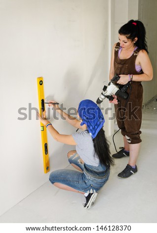 Two women renovating a house using a spirit level to mark a straight line on a wall before drilling a hole with their electric drill