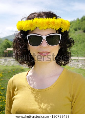 A close up portrait of a young woman smiling wearing white sunglasses, wearing a garland of yellow flowers.
