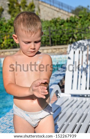 Careful little boy applying sunscreen to his skin at the swimming pool to protect himself against the summer sun
