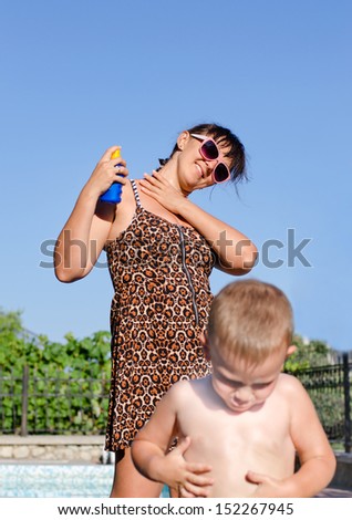 Mother and her young son applying suntan lotion to their skin to protect against ultraviolet rays as they prepare to spend the hot summer day at t their pool