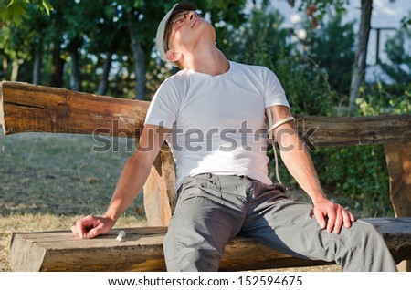 Addicted man sitting on a bench in the park feeling side effects after injecting a drug dose intravenously