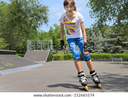 Young teenage girl roller skating at a skate park approaching the camera at speed on her rollerblades with the cement ramps of the park visible behind