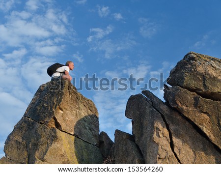 Backpacker on a distant rocky mountain peak outlined against a sunny blue sky as he goes rock climbing during his vacation