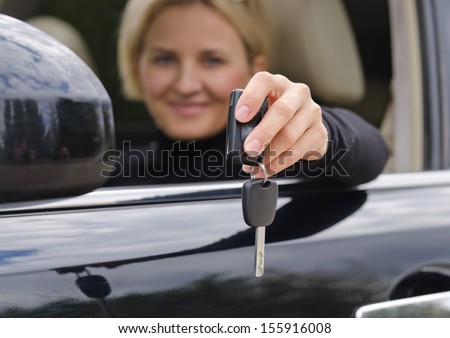 Smiling blonde woman holding a car key inside the car