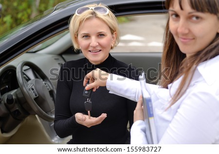 Happy saleswoman handing over car keys to the attractive blond female owner of the new car
