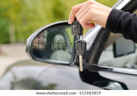Woman driver holding a set of car keys and remote control outside the vehicle depicting new ownership, success and achievement