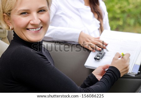 Beautiful smiling blond woman signing a contract with a saleslady that will make her the proud owner of a new car