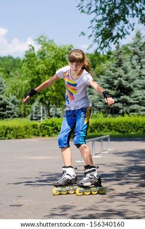 Young teenage girl in a skate park balancing on the tips of her roller blades with her hands in the air as she prepares to perform a move